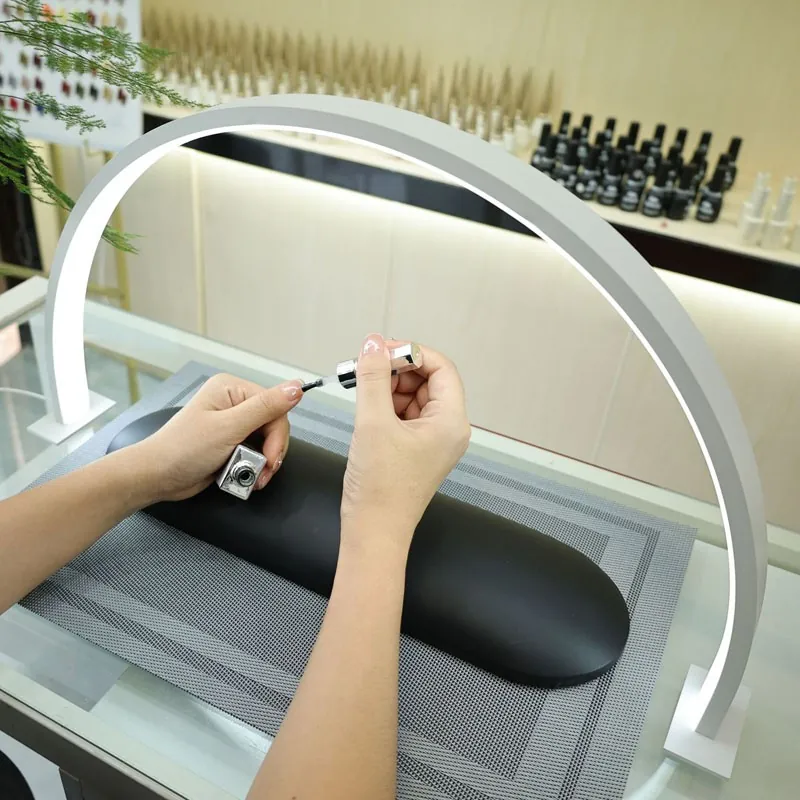 Applying nail polish on a nail table lit by a white half moon lamp